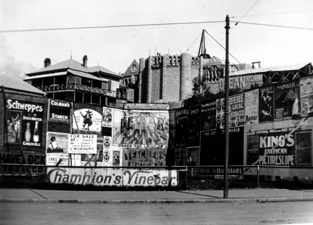 Figure 4: An incomplete St John’s Cathedral rising up behind the advertising hoardings in Queen Street, c. 1908 (State Library of Queensland).